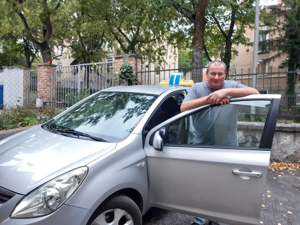 Váradi Csaba, az Apró Autósiskola oktatója az oktatóautó mellett